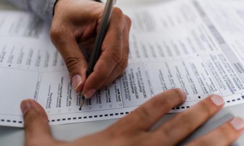 A closeup of a person's hands filling out a ballot.